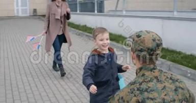美丽的妻子和儿子在户外会见军人。 快乐的小孩扔欢迎回家的海报和跑步